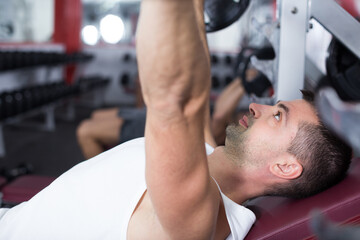 Portrait of young athletic man during training with barbell in gym
