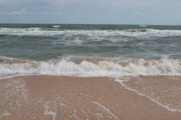View of the beach and sea with waves against the blue sky.