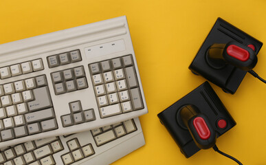 Old keyboard and joysticks on yellow background. Retro gaming. 80s. Top view. Flat lay