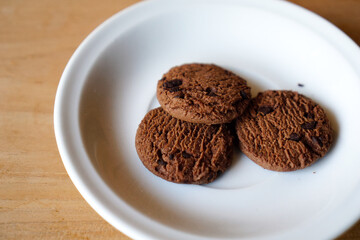 chocolate cookies and dark chocolate grain on white plate. snack theme on wooden table background