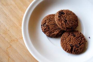 chocolate cookies and dark chocolate grain on white plate. snack theme on wooden table background