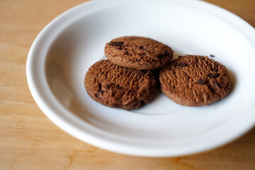 chocolate cookies and dark chocolate grain on white plate. snack theme on wooden table background