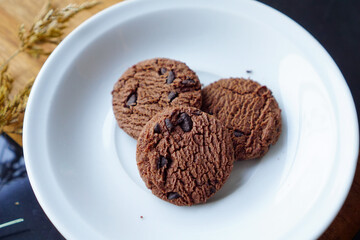 chocolate cookies and dark chocolate grain on white plate. snack theme on wooden table background