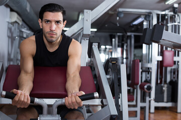 Fototapeta na wymiar Muscular man doing strength training on fitness machine in modern gym