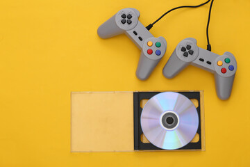 Retro gamepads, CD in box on yellow background. Gaming, video game competition. Top view, minimalism