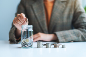 Closeup image of a businesswoman collecting and putting coins in a glass jar