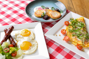 Breakfast with salad, fried egg and sausages served in white plate over red plate tablecloth.