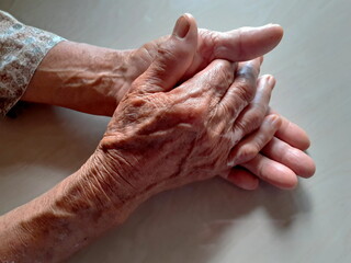 Fototapeta premium Holding hands, asian old woman, she is 70 years, with wrinkles that has a surface on smooth sheet in the background, close up concept,