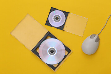 Compact disсs with boxes, retro pc mouse on yellow background. Top view