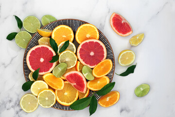 Immune boosting citrus fruit health food with orange, lemon, grapefruit &   leaves on round plate and marble background. Super foods high in antioxidants, vitamins, dietary fibre & anthocaynins.  