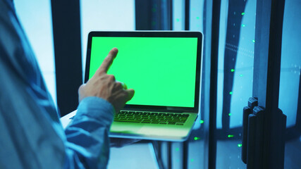Close-up of IT server administrator holding a laptop in server cabinet, working on chromekey...