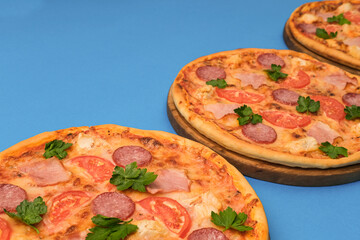 Three pizzas on the blue azure background. Pizza isolated. Banner with copy space for text or logo. Italian cuisine.