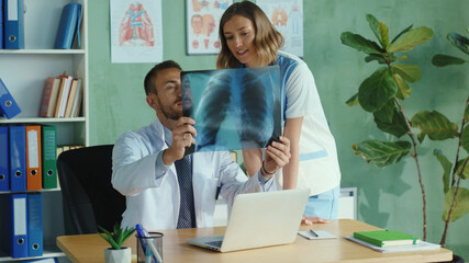 Fototapeta premium Caucasian doctor and nurse examine an x-ray lung radiography in the office. Romantic couple of doctors hug and enjoy work together at hospital. Health care. Relationships.