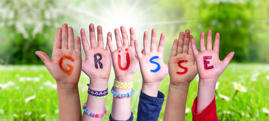 Children Hands Building Colorful German Word Gruesse Means Greetings. Sunny Green Grass Meadow As Background