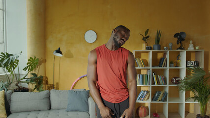 African american athletic man doing neck circles rolling his head stretching shoulders arm muscles in living room. Home training. Workout. Healthy activity.