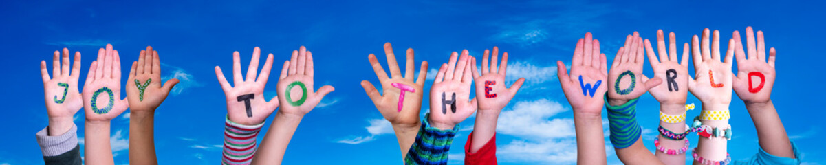 Children Hands Building Colorful English Quote Joy To The World. Blue Sky As Background