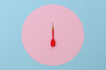Red plastic dart with metal tip on blue pastel background with pink circle. Top view. Flat lay. Minimalism