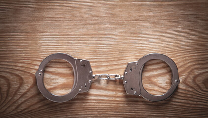 Metal handcuffs on wooden background.