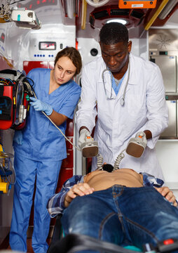 Diligent emergency doctor resuscitating male patient with help of defibrillator