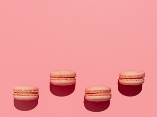 Pink macarons with copy space. Row of perfect french macarons or macaroons on pink background. Top view or flat lay. Hard light