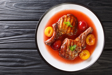Fried spicy pork chop with fresh plums and fruit sauce close-up in a plate on the table. horizontal top view from above