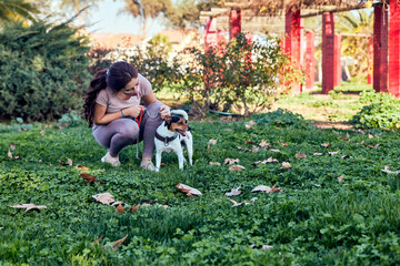 young woman wearing a safety mask in the park with her dog petting him in the middle of the covid 19 pandemic