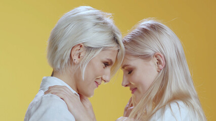 Happy together lesbian girls embrace each other telling romantic things promising giving kisses posing at orange background. LGBT love. Love and relationships.