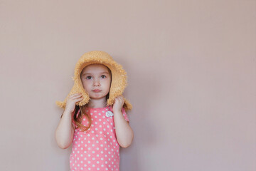 Portrait of cute little girl in straw hat in the studio on pink background. Photography concept. Copy space for text