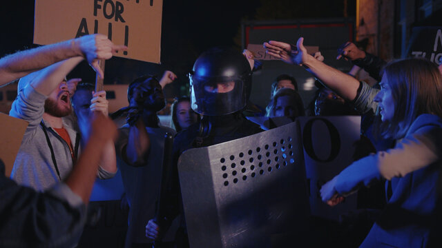 Violent street protesters fight with the policeman on street at night. Police officer trying to control and suppress strike demonstration rally. Revolution. Riot.