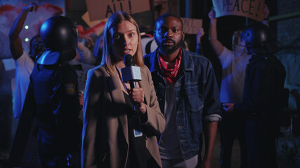 Fototapeta na wymiar Beautiful serious woman journalist making a live speech on TV explaining the situation with night street demonstration rally. No racism. Black lives matter. Shocking news.