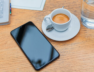 Fototapeta na wymiar Black mobile smartphone with blank screen notebook and cup of coffee mock up design on wooden table