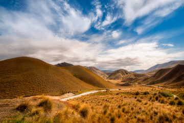 Golden light at a New Zealand Desert Mountain Pass: A two-lane highway curves through arid terrain toward Lindis Pass in Otago Region, on a beautiful summer day in New Zealand, South Island.