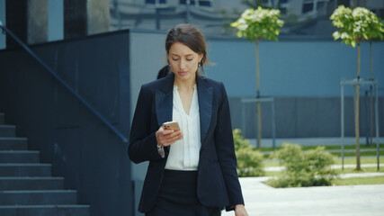 Young beautiful business manager office employee woman using mobile phone for remote communication outside corporate building. Social distance. Employment.