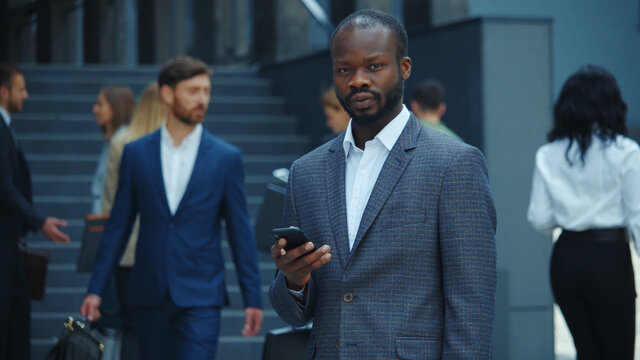 Attractive businessman afro-amercian leader executive with smartphone look at camera in business district corporate workplace. Portraits. Success. Technology.