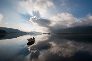 A boat on a flat mirror like lake with dramatic clouds in the mountains. 