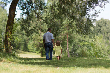 Naklejka na ściany i meble Grandfather and granddaughter walking and spending time together in nature. Copy space.