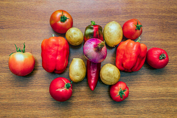 Three pods of red bell pepper, six tomatoes, fresh potatoes and onions lie on the kitchen table
