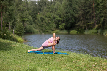  woman practicing yoga  and engaged in stretching on the shore of the lake on a summer day.  solo outdoor activities. Social Distancing. copy space
