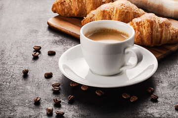 cup of coffee and croissants standing  on wooden board placed on old rustic background