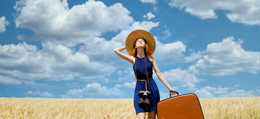 Redhead girl with suitcase at spring wheat field.