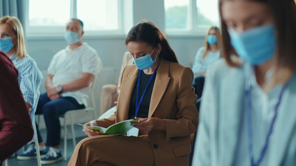 Business seminar. Quarantine. Attentive multi-ethnic corporate men and women with masks listening to business lecture presentation in conference meeting room. Social distancing.