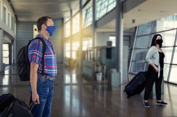 A man and a woman wearing protective face masks go to the check-in terminal at the airport. Everyone carries a black suitcase.