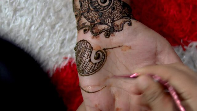 Closeup of Woman designing Henna or Mehendi Tatto on the palm of a girl