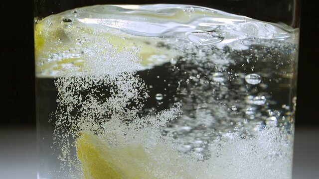 Wedge of lemon dropped from top of frame into a glass of carbonated water with 1 lemon wedge floating - SLOW MOTION 240 frames per second (240p 240fps) - Shot in 2K exported as 1080p