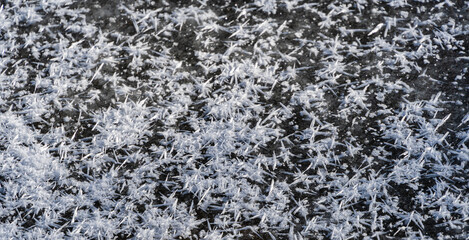 Natural ice structure on surface of frozen and snow-covered pond. Beautiful ice patterns are covered with snow. Close-up. Snowflakes on icy surface of the pond. Nature concept for winter design.