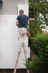 Carpenter standing on a ladder and working on a house exterior