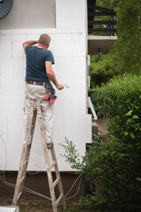Carpenter standing on a ladder and working on a house exterior