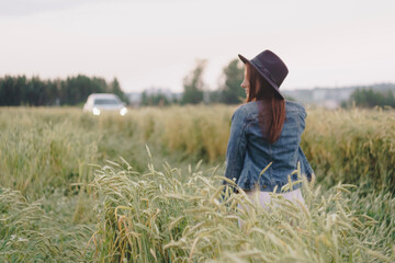 Naklejka na ściany i meble Beautiful young girl in a denim jacket in a green field of rye at sunset