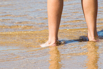  pies masculinos mojándose en la orilla de la playa y arena dorada
