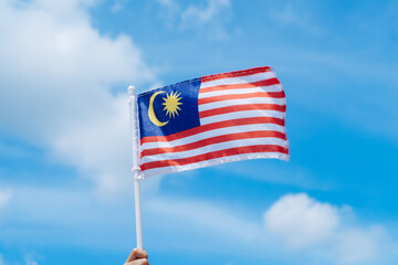 Hand happily waving Malaysia flag against blue sky.